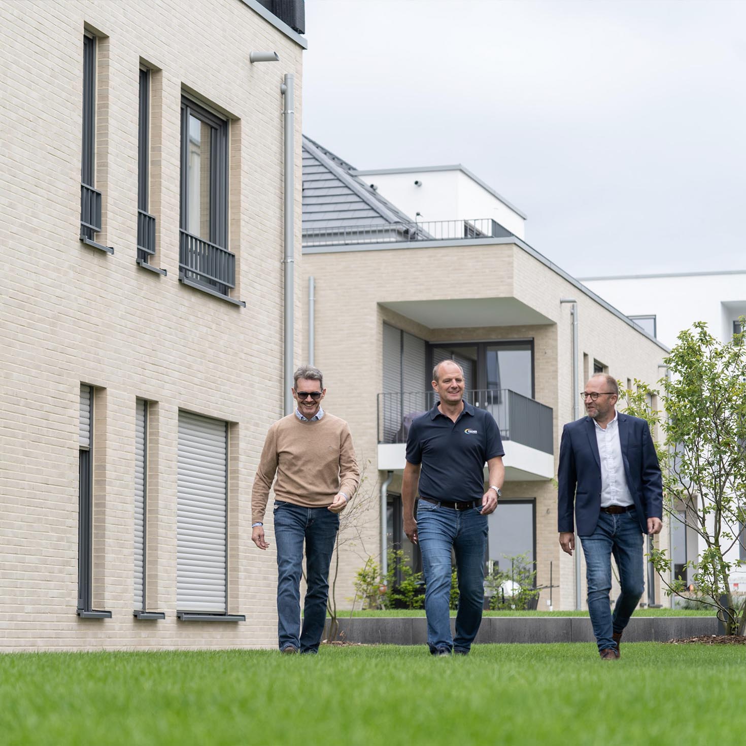 Drei Männer laufen vor einem Haus über den Rasen